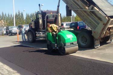 Asphalt roller compacts fresh asphalt in front of dump truck