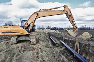 Excavator lowers large pipes into long industrial trench