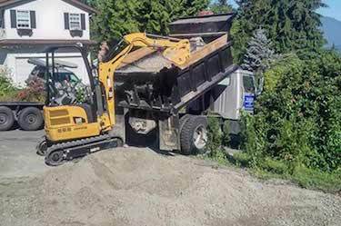 Mini excavator taking dirt from back of Valroc dump truck
