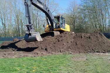 Large excavator on top of soil pile